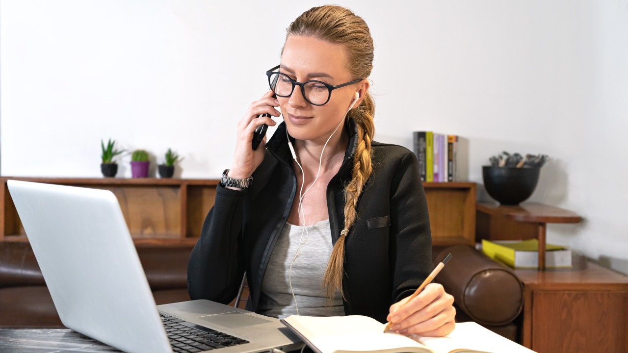 cursos gratuitos. Una mujer hablando por teléfono mientras va tomando nota